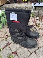 Side view of tall black Kamik winter boots with quilted upper and buckle detail, showing brand logo and size tag 11