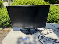 Front view of 23 inch black ViewSonic LCD monitor with power and VGA cables attached, showing screen and stand on table outdoors.