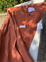 Overall view of rust-colored curtain draped on a surface showing color and fabric texture.