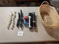 Full view of marble chess pieces, collapsible swords, juggling ball and wicker basket on table.