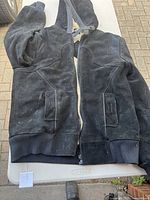 Black suede men's winter jacket laid flat showing front zipper, ribbed cuffs and two front pockets.