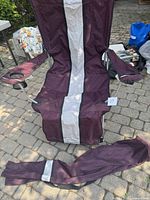Front view of the maroon and gray waterproof fabric chair with its carrying bag laid in front of it on a stone floor outdoors.