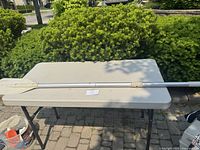 Full length view of the Quicksilver paddle placed on a table outdoors showing the aluminum shaft and sectioned design.