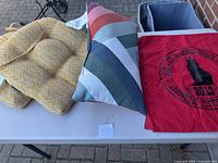 Two yellow seating cushions and one multicolored decorative pillow plus a red bandana laid on a table outdoors.