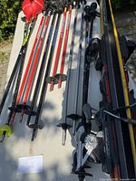 Wide view of pairs of skis and numerous ski poles laid out on a table outdoors under sunlight