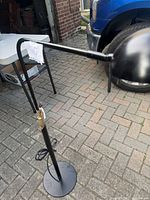 Black floor lamp standing outside, showing full lamp structure including round weighted base and adjustable arm with cylindrical shade.