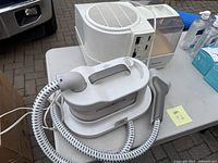 White Rowenta Pro Compact clothes steamer with handheld steam iron and base unit on table outdoors.