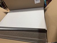 View of white corrugated cardboard sheets stacked in a box, showing thickness and quantity.