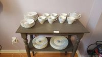 Full set arranged on brown side table showing dinner plates, smaller plates, cups, and saucers all with blue rose pattern.
