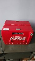 Front view of red Coca-Cola cooler radio, showing brand text and radio dial.
