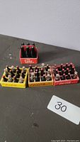 Four miniature crates in yellow, orange, and red each holding six mini glass Coca-Cola bottles with visible caps