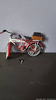 Coca-Cola model bicycle collectible with a crate of mini bottles mounted on rear rack, pedal is broken off, with a small key lying in front.