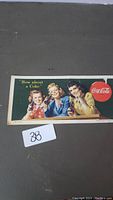 Front view of vintage Coca-Cola advertising sign showing three women, slogan, and logo