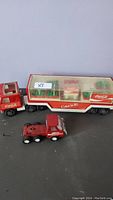 Overall view of the two Coca-Cola toy trucks, the larger one with trailer and mini bottles and the smaller red truck cab
