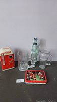 All Coca-Cola items displayed including the mini vending machine tin, glass bottle, two glasses, and card deck tin.
