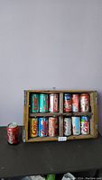 Wooden crate filled with vintage Coca-Cola cans with one can placed outside on the left side.