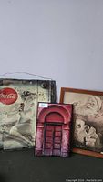Full view of three advertisements including the metal Coca-Cola sign, framed Santa Claus print, and red door plaque.