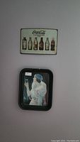 Small rectangular Coca-Cola metal sign showing various historic Coke bottles on a white background