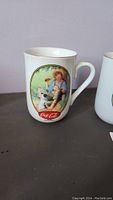 Photo showing first mug with Norman Rockwell painting of boy and dog drinking Coca-Cola, 22K gold trim