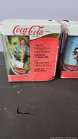 Photo showing original Coca-Cola branded box with text confirming 22 karat gold trim and Norman Rockwell artwork.