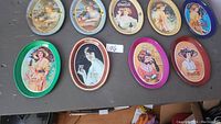 Nine mini Coca-Cola trays laid on a dark surface, showing vintage themed artwork of women holding or drinking Coca-Cola, metal trays with colorful vintage designs.