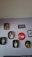 Seven vintage Coca-Cola metal advertising trays hanging on a lavender wall, displayed in an asymmetrical pattern.