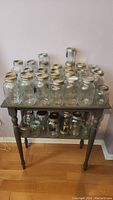 Front view of many clear glass jars arranged on two-tiered wooden table.