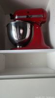 Red KitchenAid tilt-head mixer on shelf with stainless steel bowl