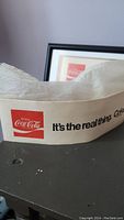 Close-up of one Coca-Cola paper hat with red logo and wording 'It's the real thing. Coke.'