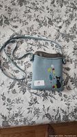 Front view of blue vegan leather purse with black cat and flowers embroidered on front.