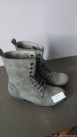 Side view of gray vegan leather boots showing lace-up front and pull tabs at the back.