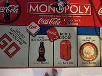 Close-up of Coca-Cola Monopoly game board corner showing Property spaces with vintage Coca-Cola bottle and item prices.