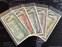 Five Canadian banknotes from 1954 lying fanned out showing the front side with Queen Elizabeth II portrait.