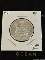 Reverse side of 1961 Canadian 50 cent coin showing Canadian coat of arms, mounted in white cardboard holder with handwritten details.