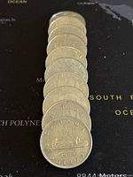 Front and back of 10 stacked Canadian silver dollar coins from 1968-1986 showing obverse Queen Elizabeth II and various reverse designs including the 1968 Voyageur Canoe design