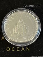 Obverse side of 1976 Canadian Silver Dollar showing Parliament Library image, inscription 'CANADA DOLLAR' and dates '1876-1976'. Coin in protective case.