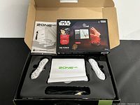 Opened box showing white Zone 40 gaming console with two white controllers, Star Wars The Force Coding Kit box and motion controller inside packaging.