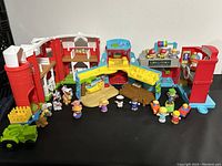 Shows overall assortment of Fisher-Price Little People lot with barn, playsets, figures, and vehicles