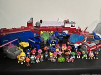Front view showing all Paw Patrol figurines in front and larger vehicles behind including fire truck, police trucks, helicopter, and assorted characters.