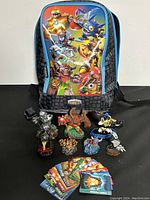 Front view of Skylanders backpack with multiple Skylanders character figures and a spread of game cards placed in front.