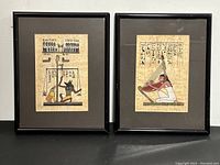 Two framed Egyptian papyrus paintings side by side on a neutral backdrop