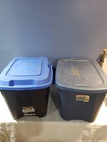 Photo of two storage bins side by side, one black with blue lid and one blue bin with lid