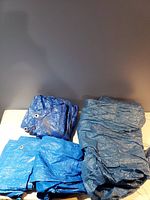 Four folded plastic tarps in different blue shades displayed on a table showing texture and metal grommets in corners.