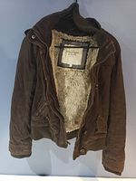 Brown jacket hanging on hanger, displaying fleece interior and exterior details including pockets and cuffs.