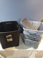 Stack of three light gray plastic storage bins with lids and a small shallow tray on top.