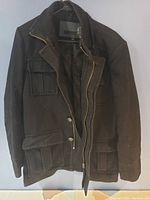 Full view of dark brown men's jacket showing front with zip and button closure, four flap pockets, and textured fabric.
