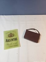 Small brown leatherette handbag and green glass tray side by side on white surface.