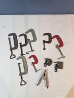 Photo showing eight clamps of various sizes and types arranged on a white surface.
