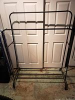 Full front view of the black metal clothes rack with double hanging bars and lower shelf for shoes or other items.