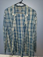 Front view of blue, white, and yellow plaid men's shirt by Eddie Bauer hanging on a black hanger.